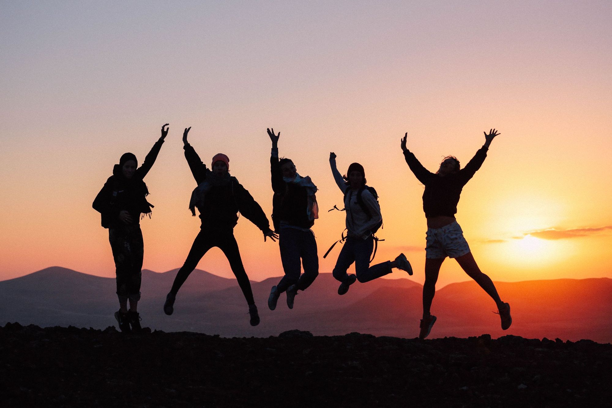 Silhouettes of five friends leaping into the air together at sunset