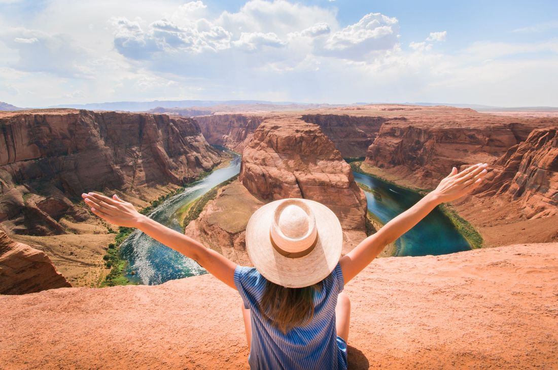A woman in a sun hat with arms spread wide at a canyon overlook