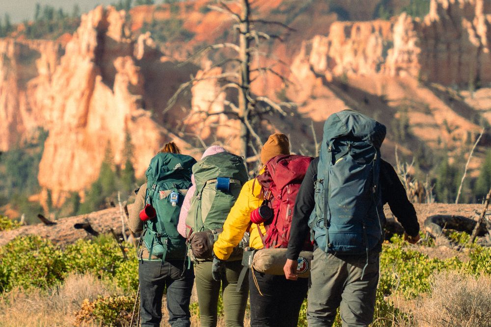 Four hikers with backpacks walking toward red rock hoodoos
