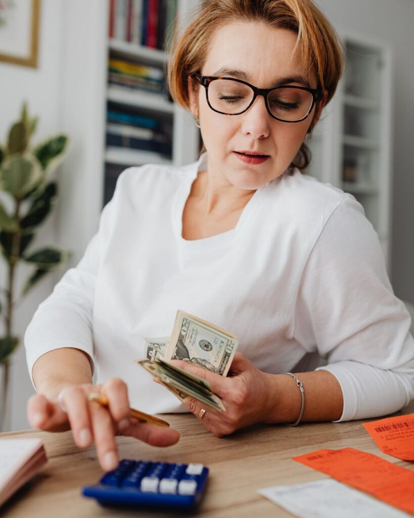 Woman in glasses adding up receipts on a calculator with cash in her hand
