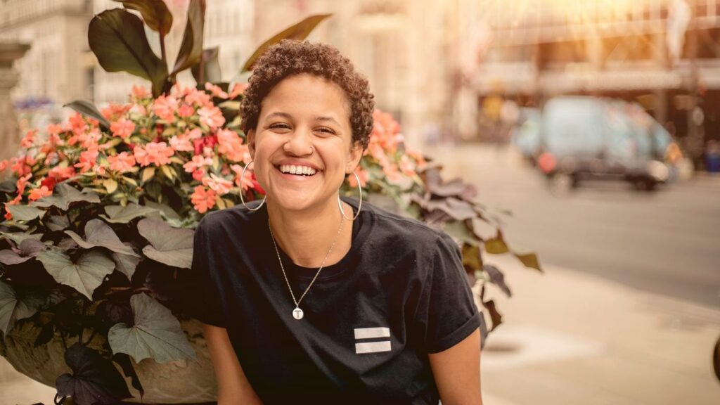 Woman smiling broadly beside a planter of flowers on a sunny city street