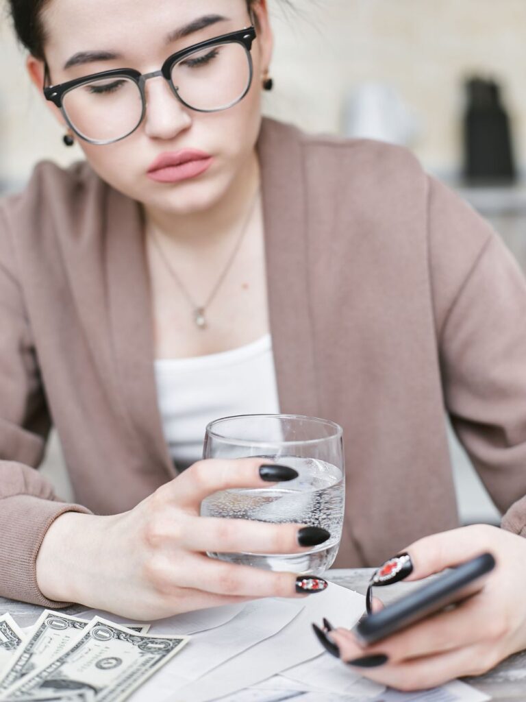 Woman checking her phone with bills and cash on the table in front of her