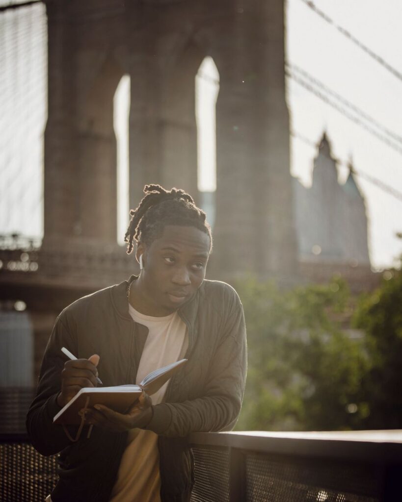 Man jotting notes in a notebook on the waterfront near the Brooklyn Bridge