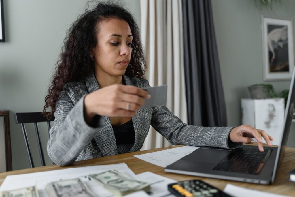 A woman at a desk with a credit card, laptop, calculator, papers and U.S. cash