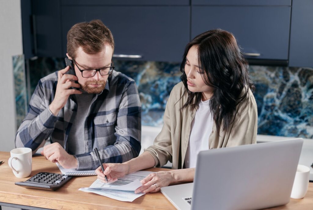 A man on the phone while a woman fills out a form at their kitchen table, checking benefits they may qualify for