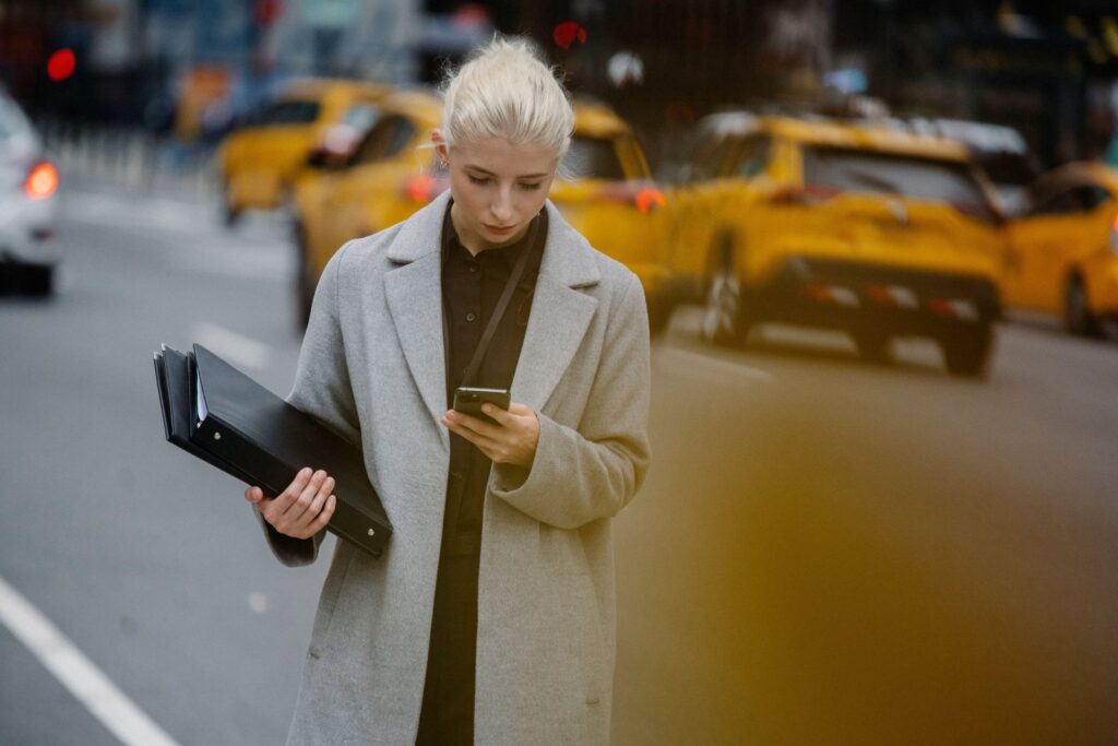 A woman on a New York street checking her phone for buy now pay later late fees and due dates
