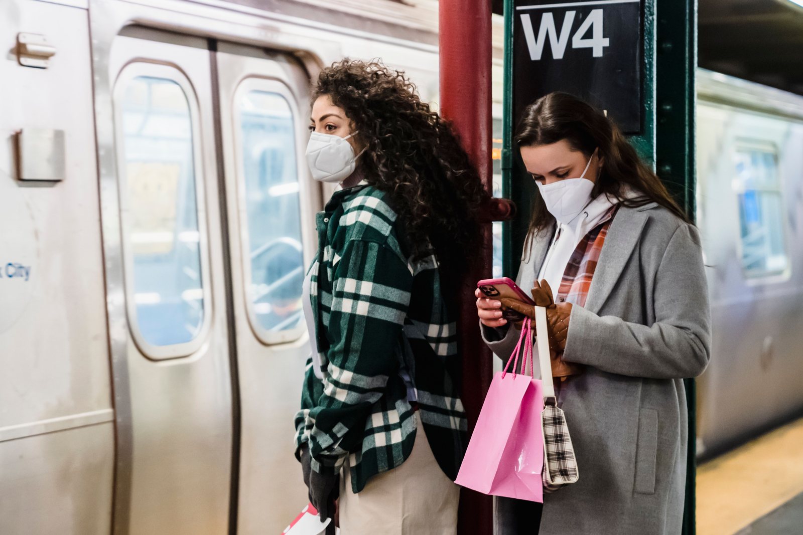 Two friends with shopping bags checking a phone on a New York City subway platform