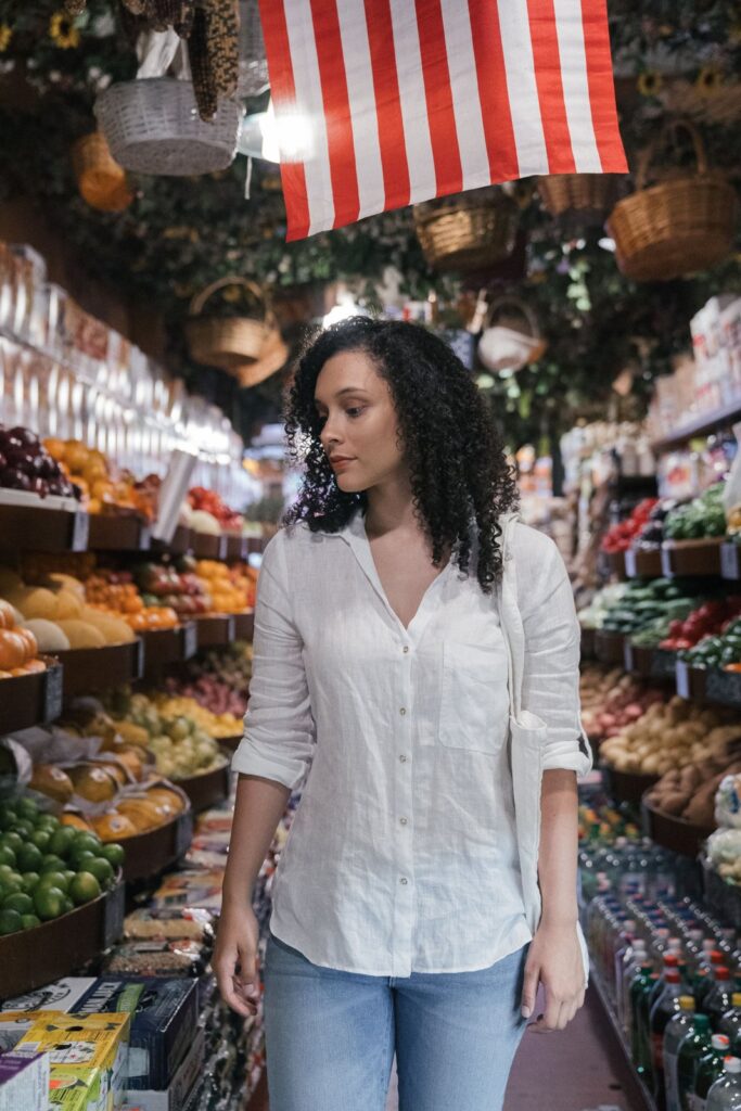 A woman walking down a grocery store produce aisle, shopping only for the gaps on her cheap grocery list for a week