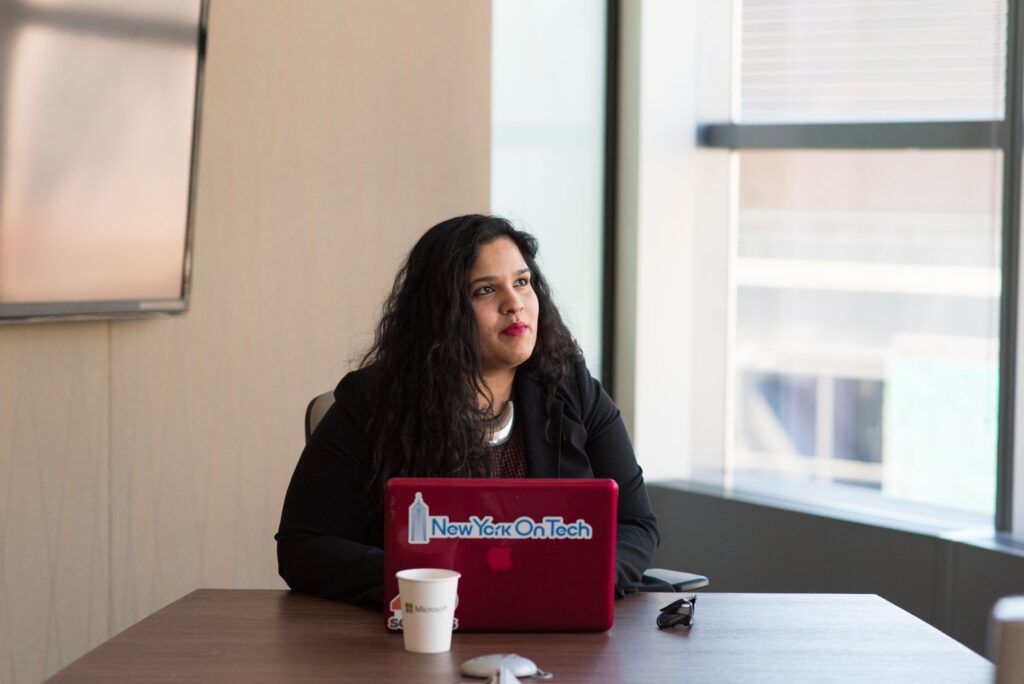 A woman sitting at a red laptop in a New York office, pausing to think, as you might when you check your credit report for free