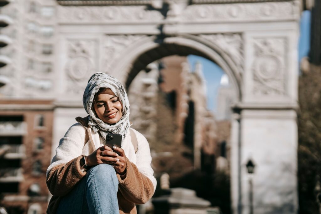A young woman smiling at her phone in a city square, the kind of moment you could use to find all your subscriptions