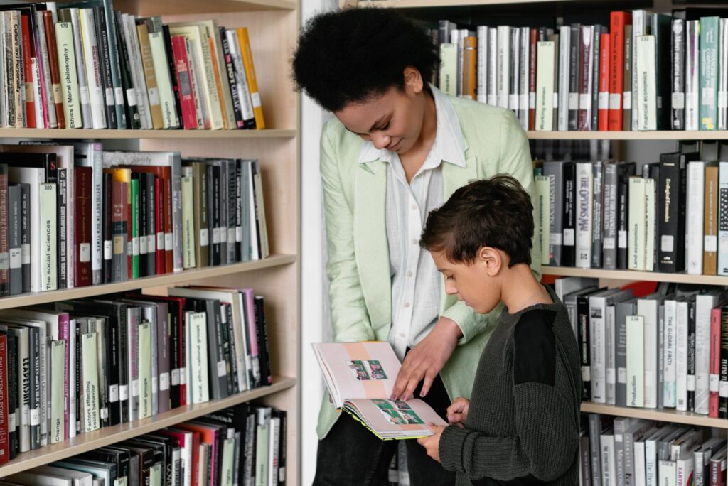 A woman showing a boy a picture book between library shelves, one of the free things to do this weekend with family