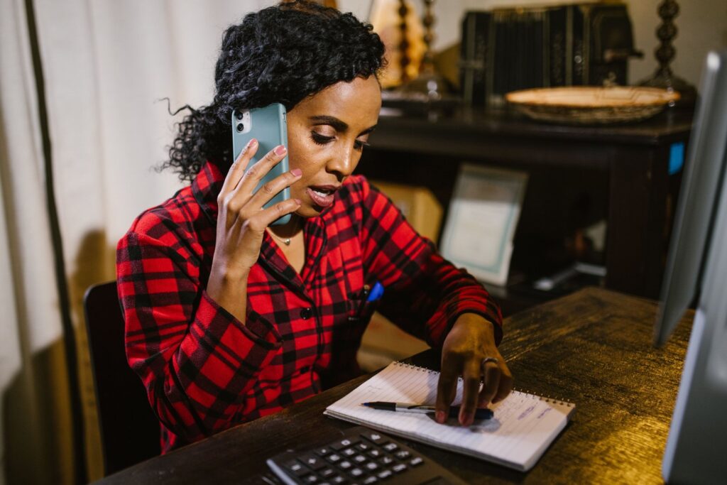 A woman on the phone taking notes in a notebook while she asks questions about how to negotiate medical bills
