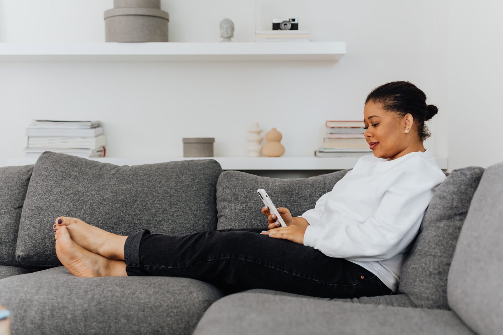 A woman relaxing on her living room sofa and scrolling her phone, the moment social media can make you compare yourself to others financially