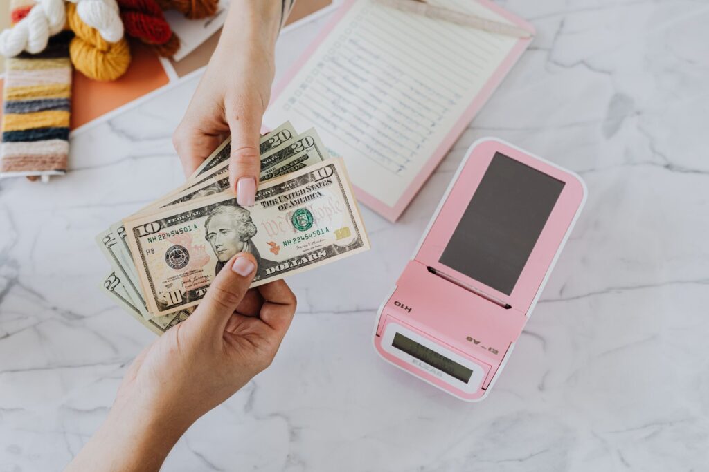 One hand passing U.S. dollar bills to another, paying in cash instead of using a credit card