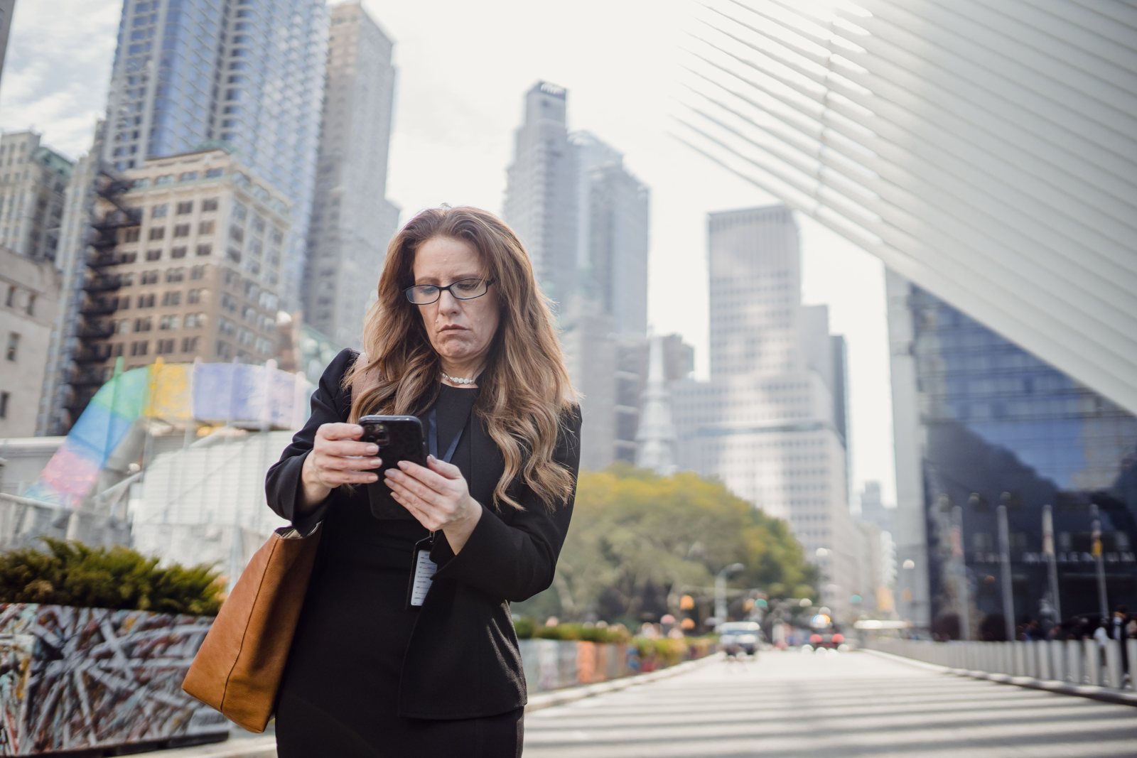 A woman in glasses standing on a New York City street, looking closely at her phone