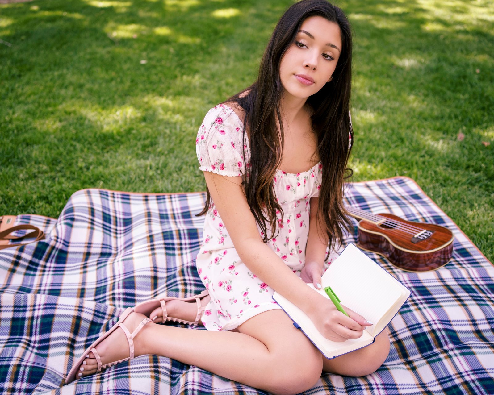 A young woman journaling on a picnic blanket in a San Francisco park, pausing to think about what financial freedom means to her