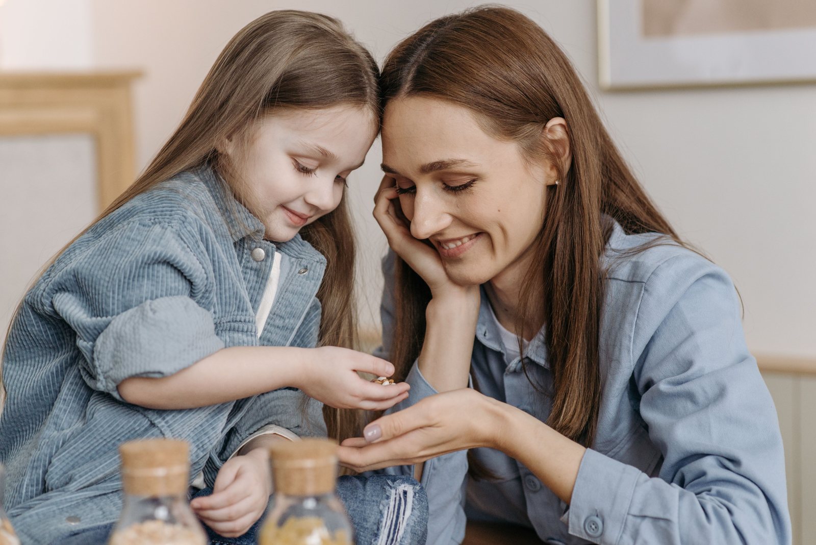 A smiling mother and young daughter sharing coins from small glass jars at home